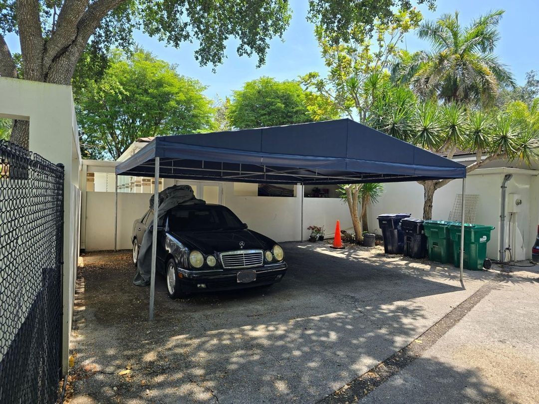 A car is parked under a canopy in a driveway.