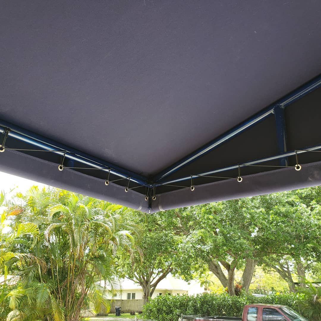 A truck is parked under a canopy with trees in the background.