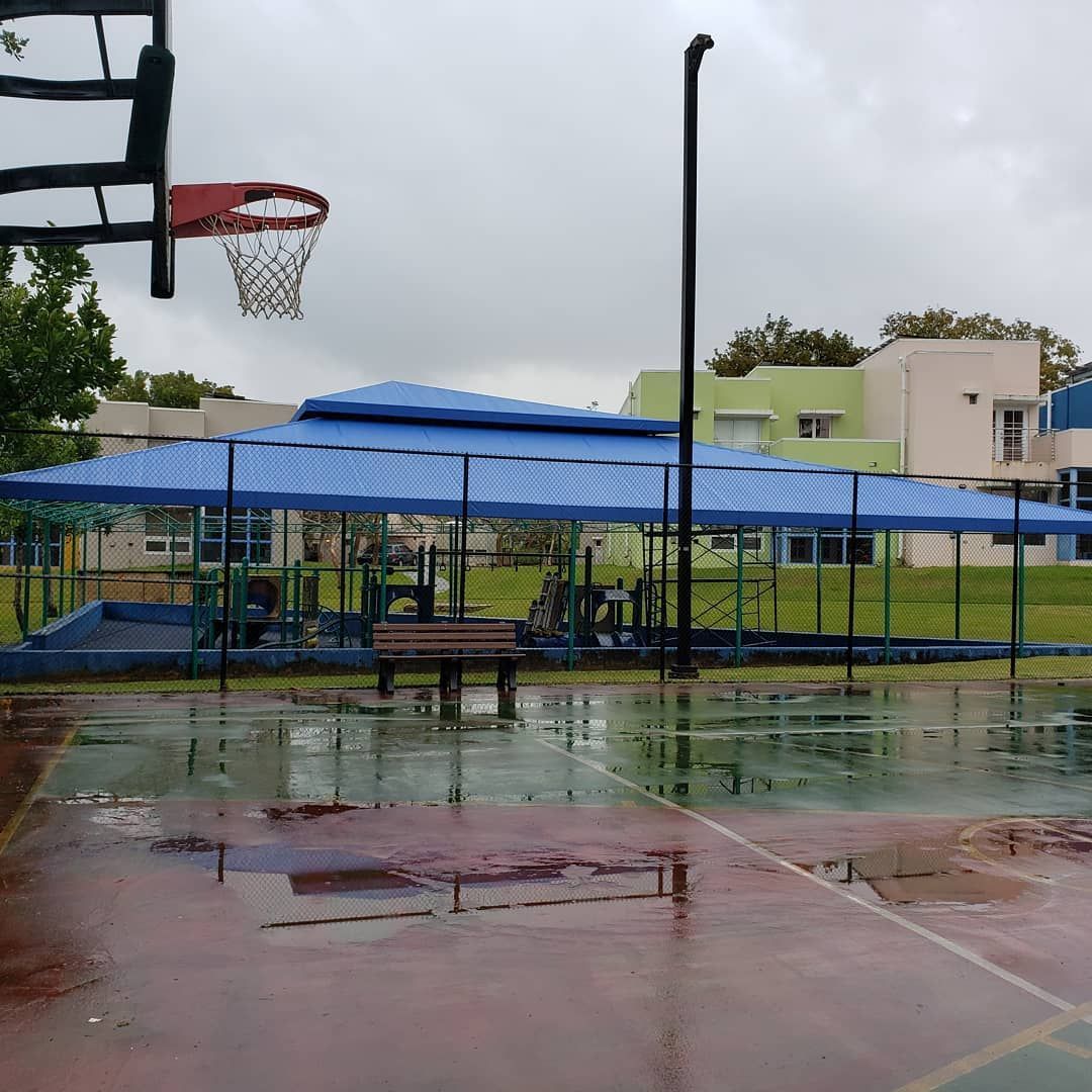 A basketball court in the rain with a blue umbrella over it