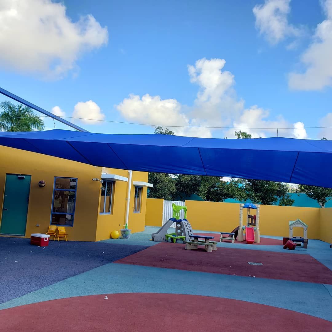 A blue canopy over a playground with a yellow building in the background