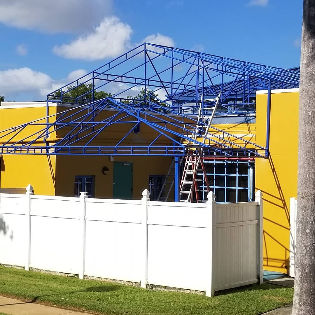 A yellow building with a blue roof and a white fence