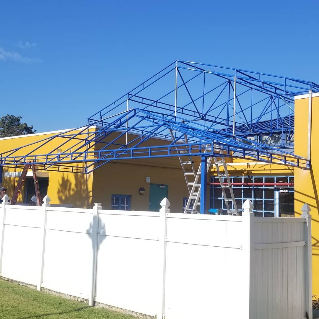 A yellow building with a blue roof and a white fence
