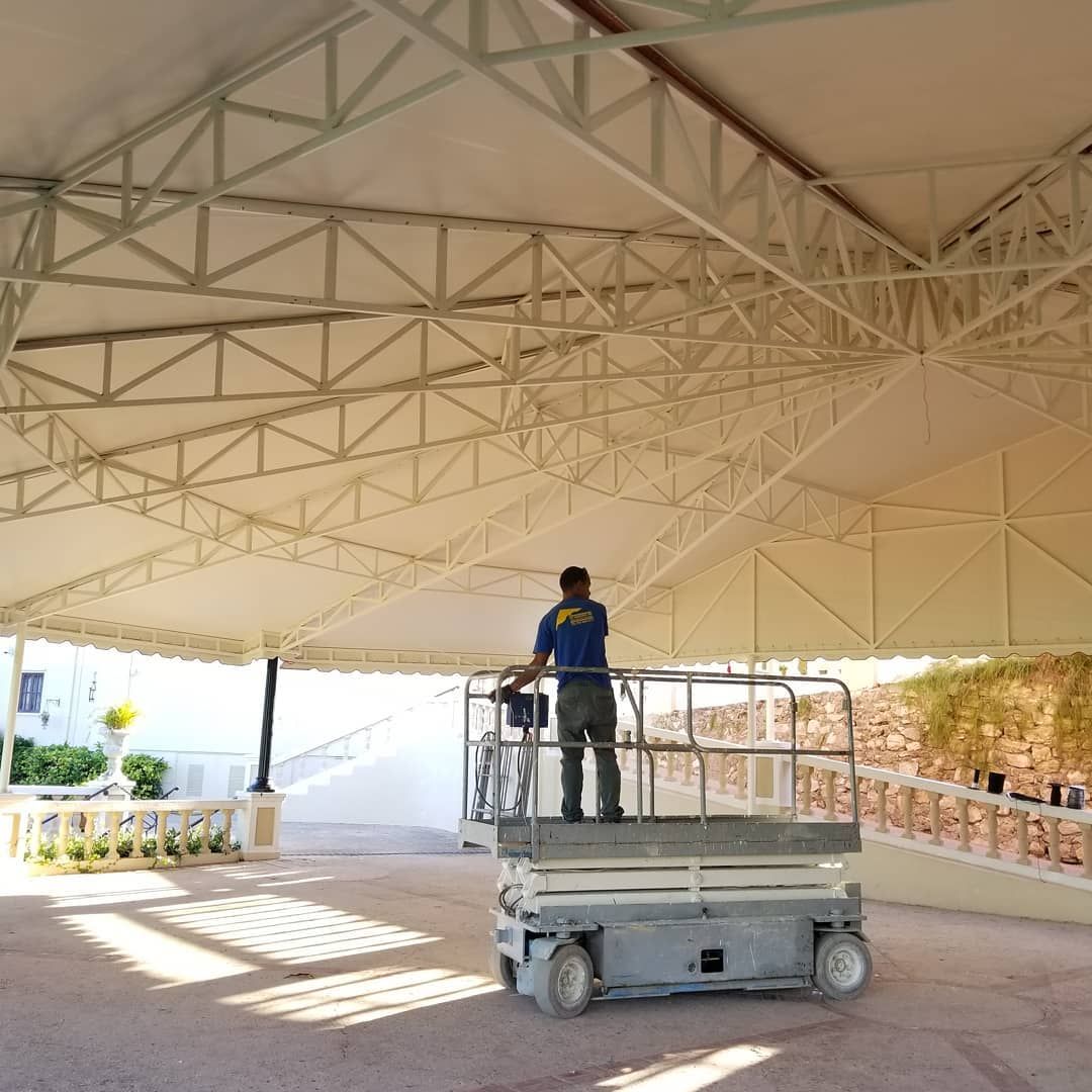 A man is standing on a scissor lift under a canopy