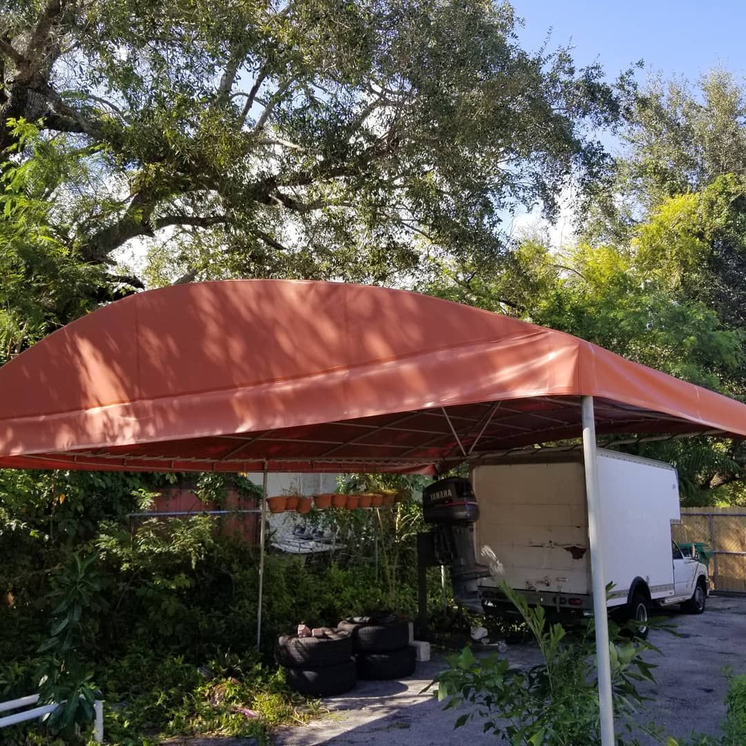 A red canopy is covering a white trailer in a driveway.