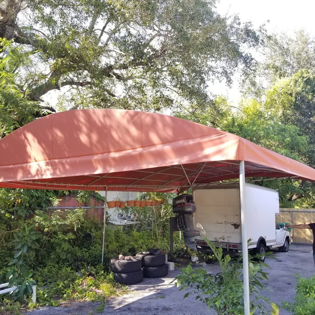 A white truck is parked under a red canopy in a driveway.