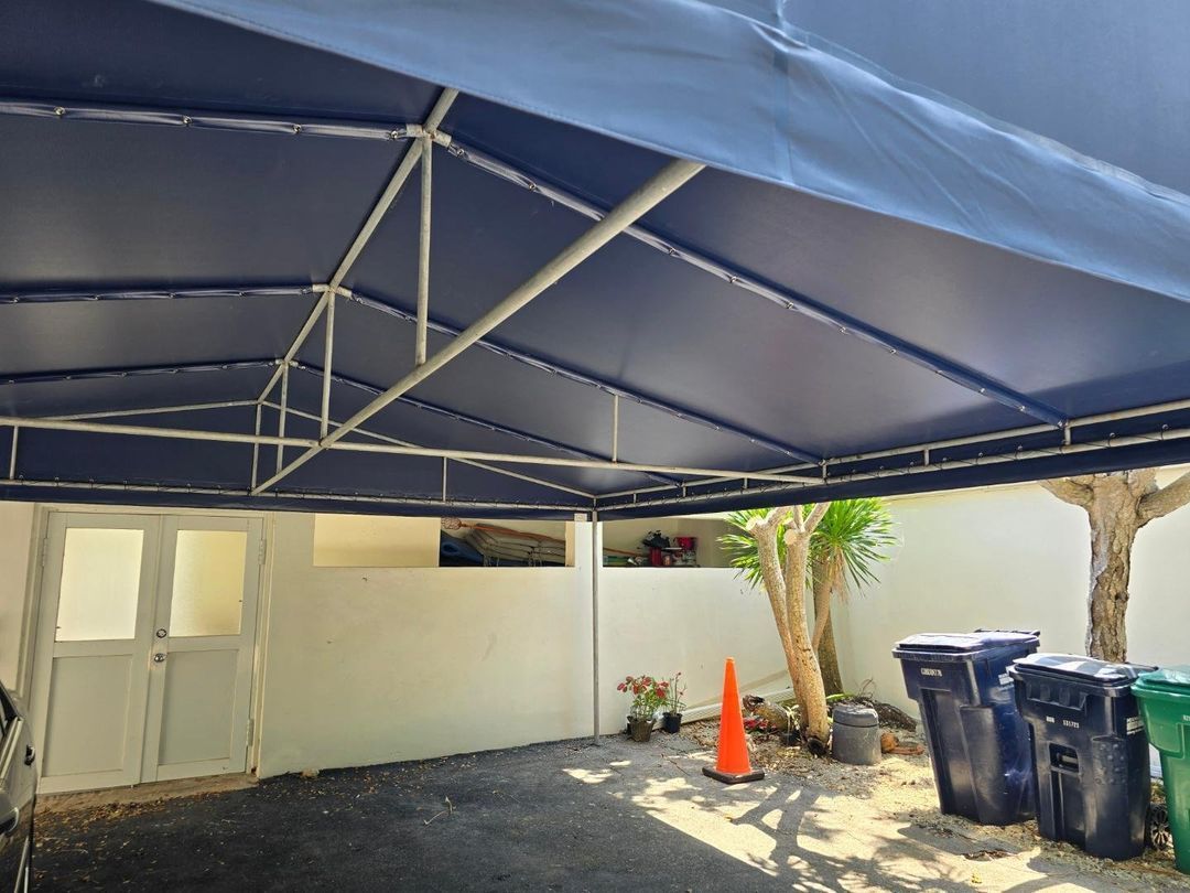 A blue tent is sitting in a parking lot next to trash cans.