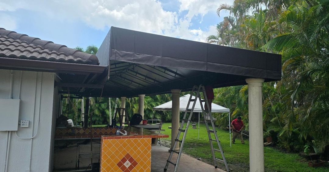 A man is standing on a ladder under a canopy in front of a house.