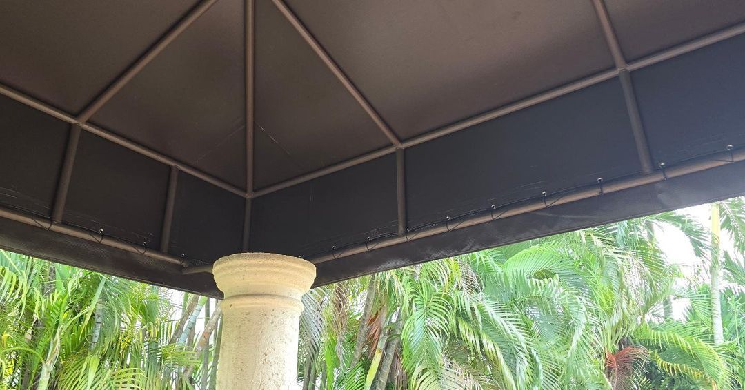 A gazebo with a roof and a pillar in the middle of a forest.