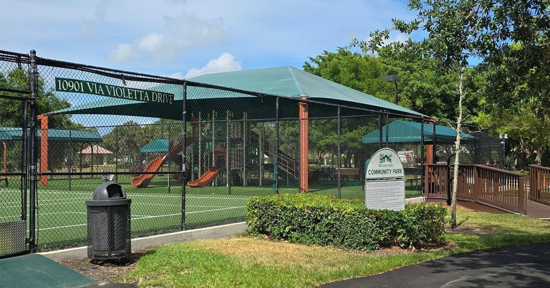 A park with a playground and a trash can in the foreground.