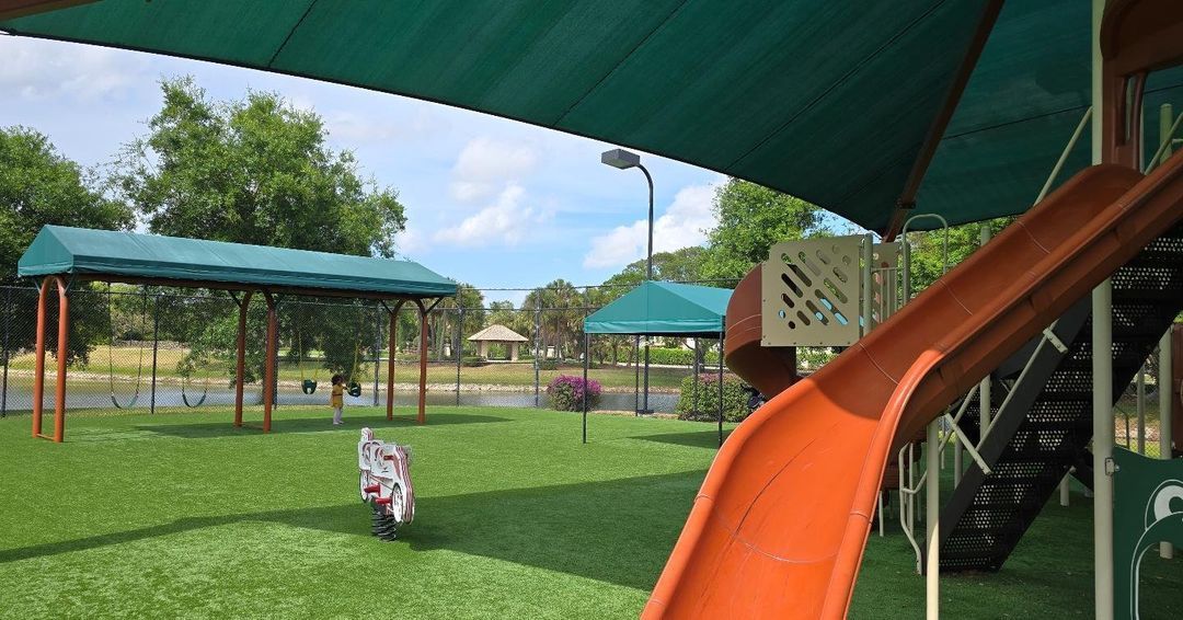 A slide in a playground with a green canopy over it.
