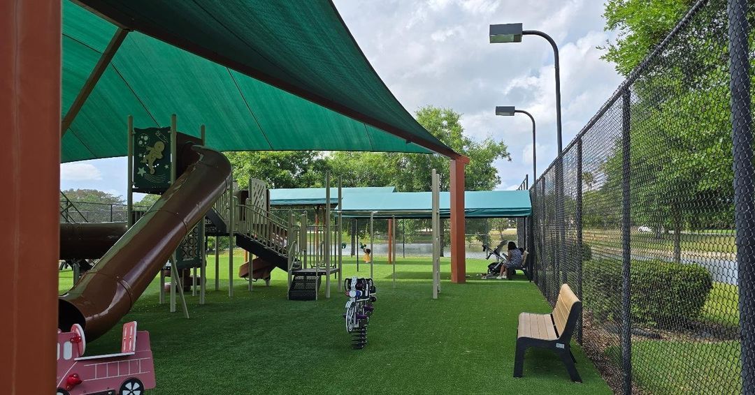 A playground with a slide and a bench under a shade.