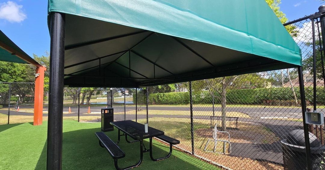 A picnic table under a green canopy in a park.