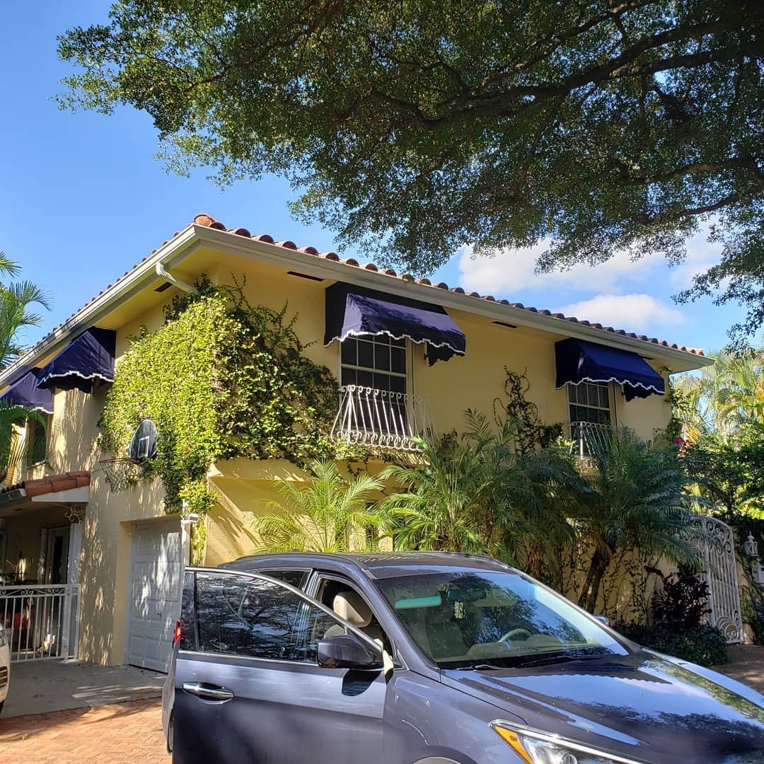 A car is parked in front of a house with blue awnings on the windows