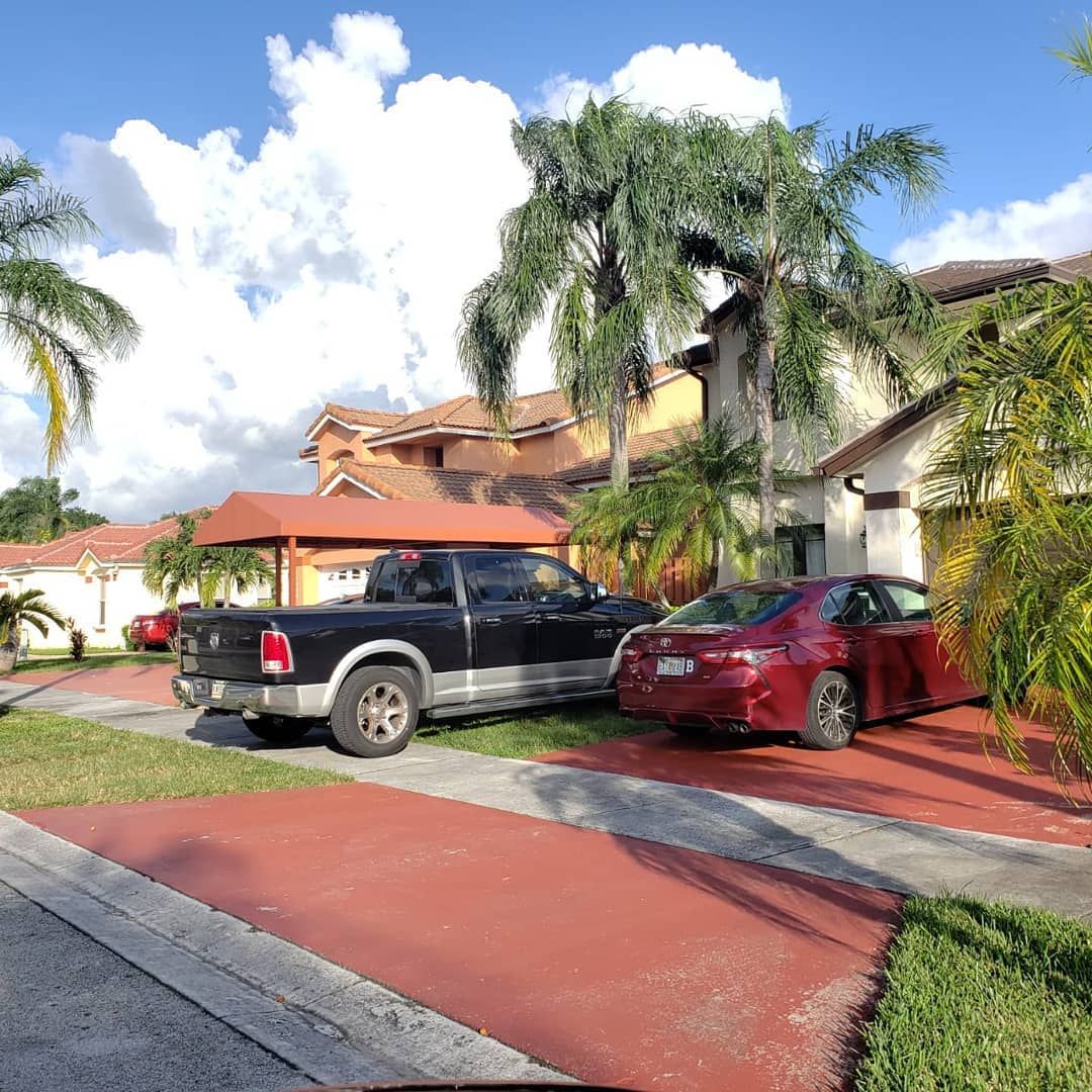 A black truck and a red car are parked in a driveway in front of a house.
