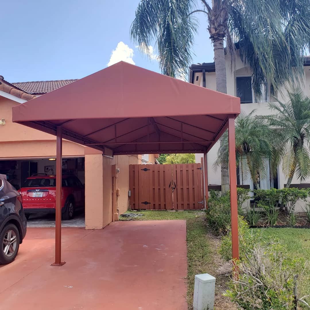A car is parked under a canopy in front of a house.