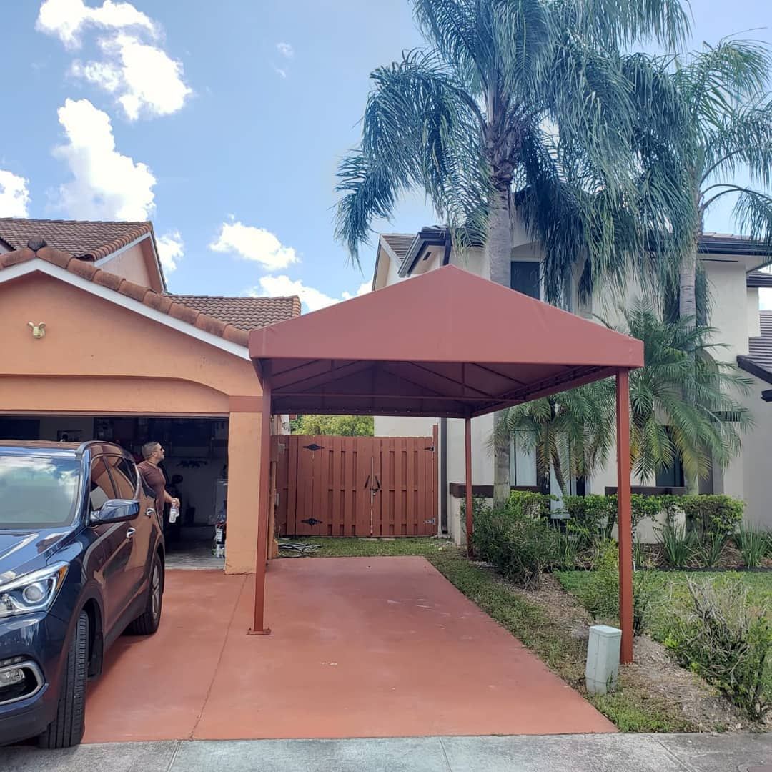 A car is parked under a canopy in front of a house.