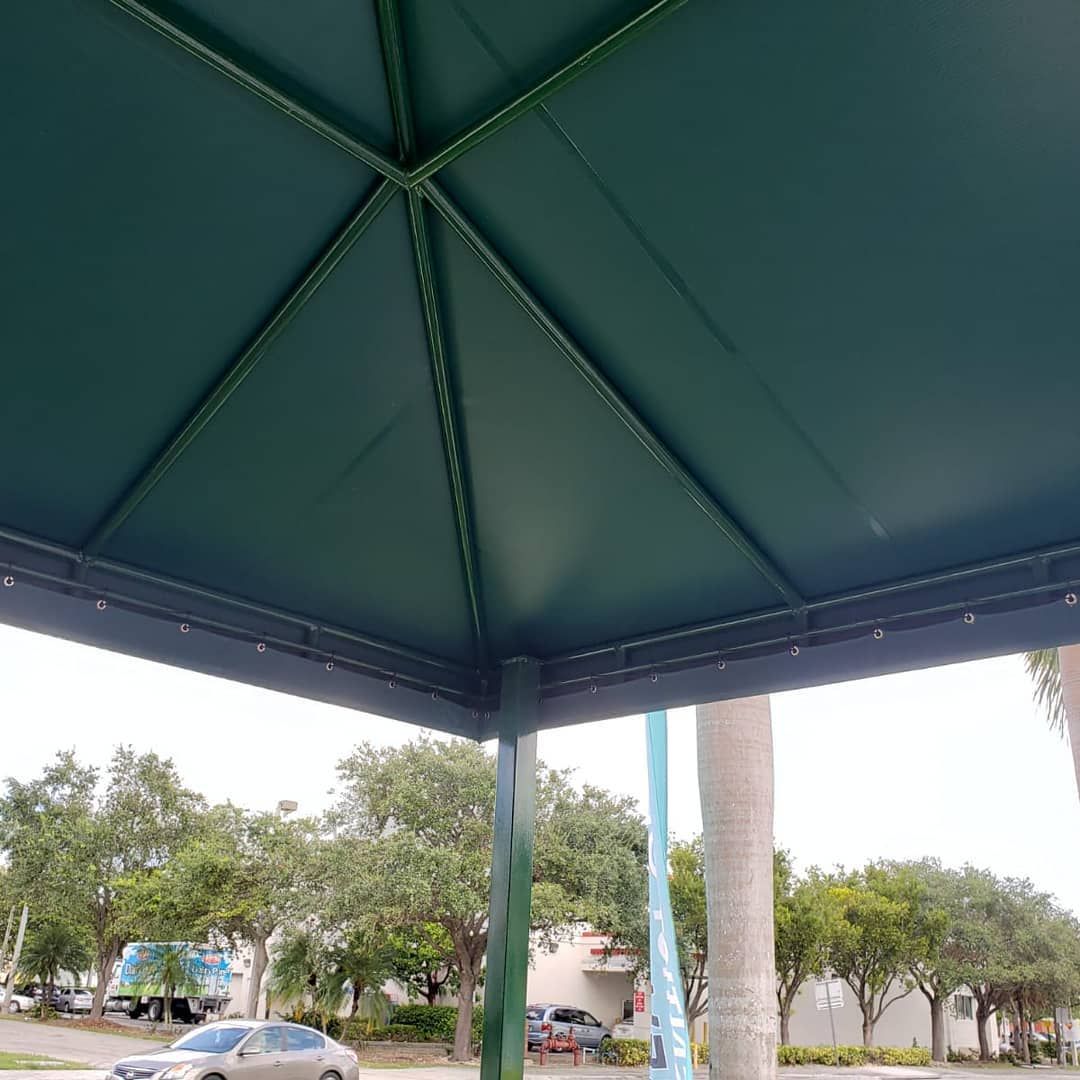 A car is parked under an umbrella in a parking lot.