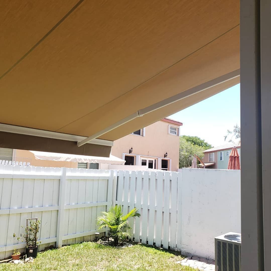 A backyard with a white fence and a brown awning