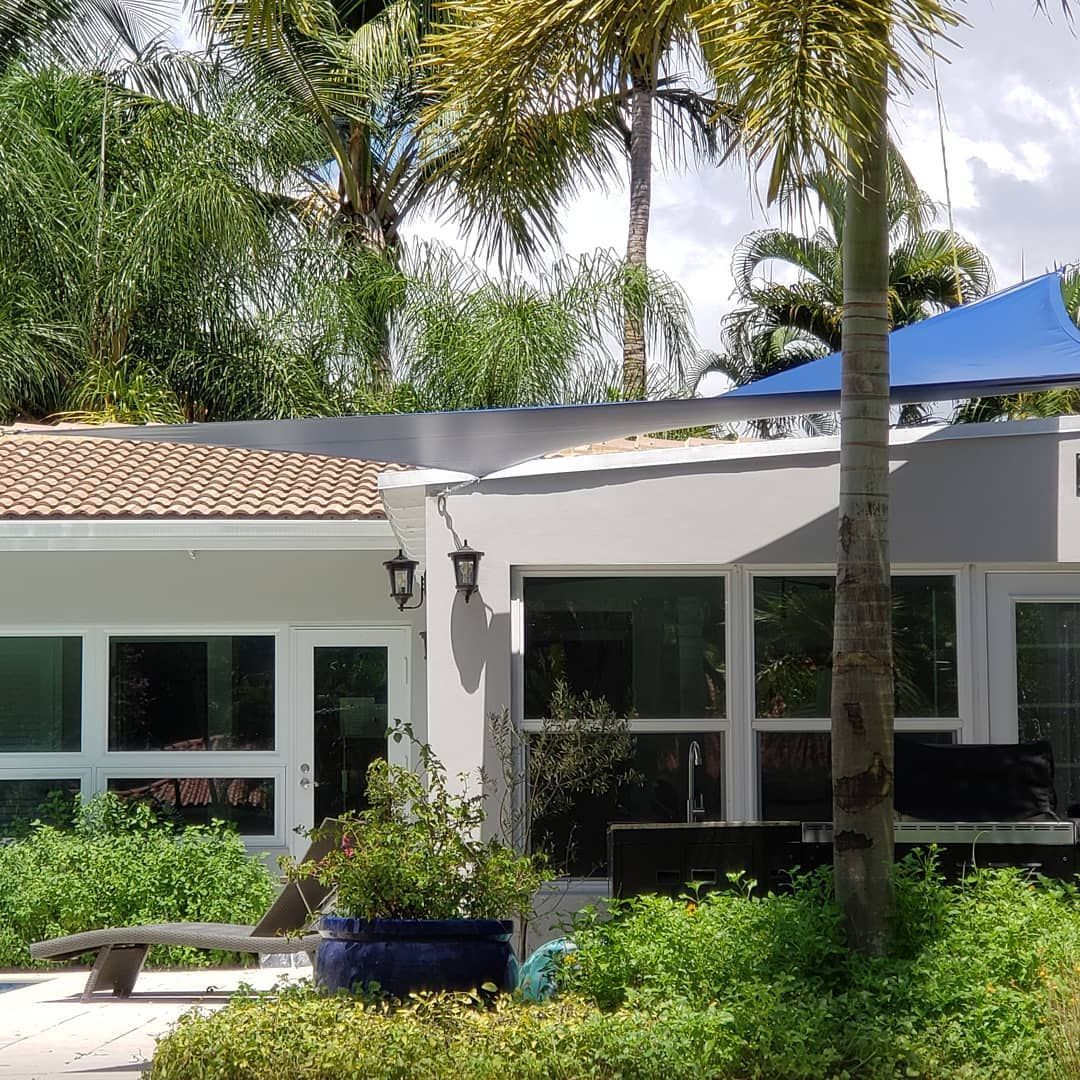 A white house with a blue umbrella and palm trees in front of it.