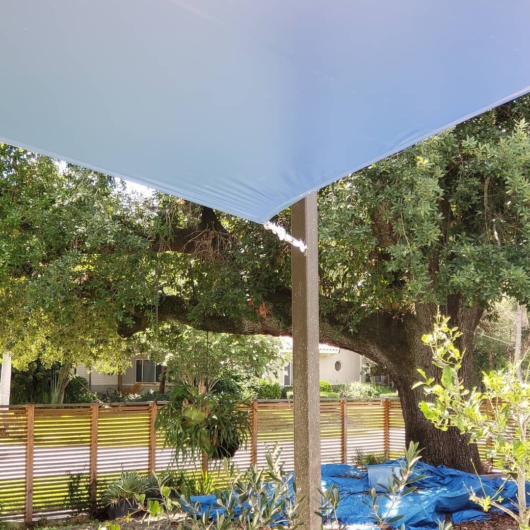 A blue umbrella is sitting under a tree in a garden.