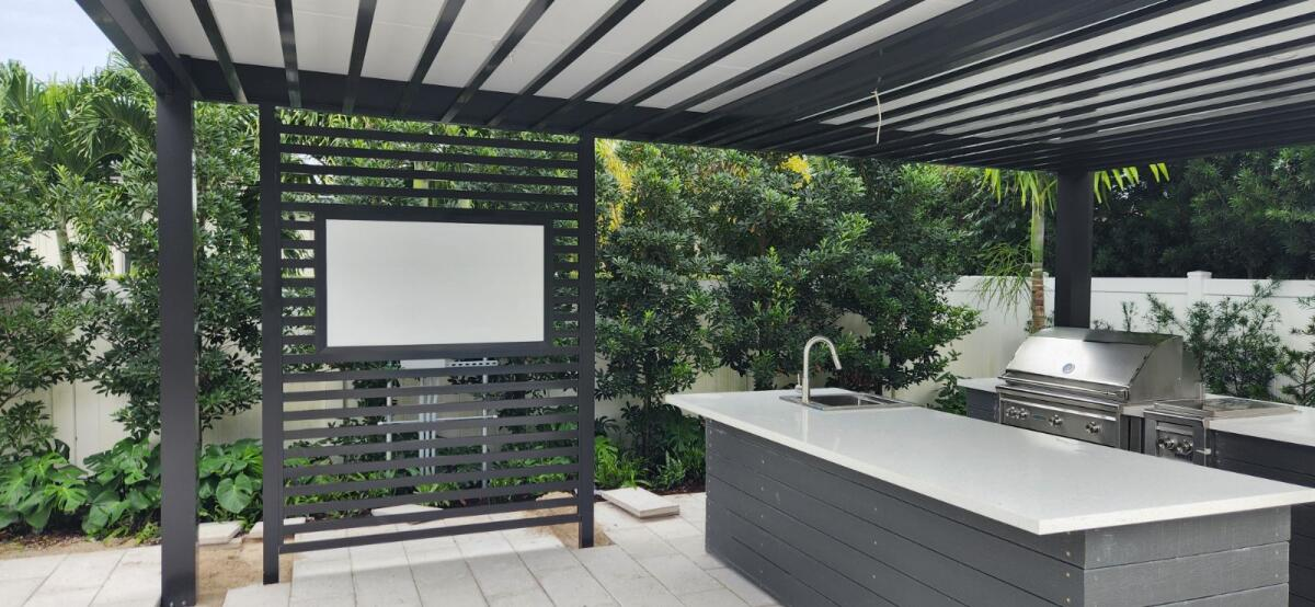 A patio with a kitchen and a television under a pergola.