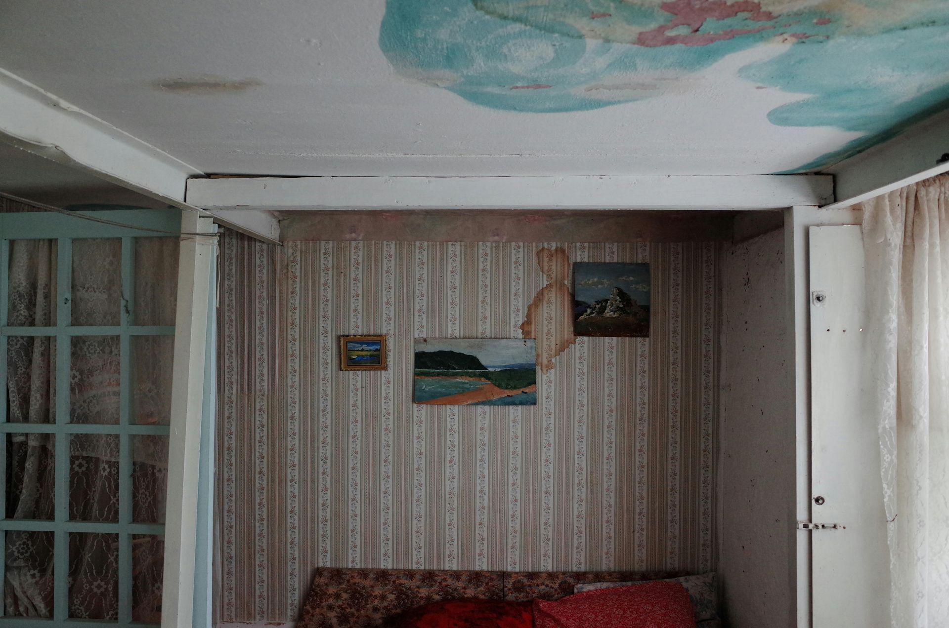 Interior room with a bed, wallpaper, artwork, and a partly painted ceiling.