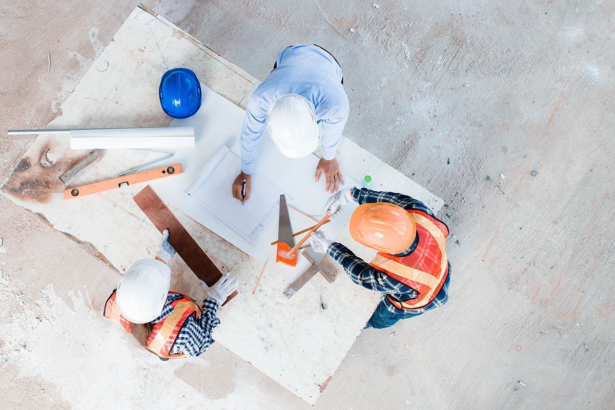 Eine Gruppe Bauarbeiter sitzt an einem Tisch und schaut sich einen Bauplan an.
