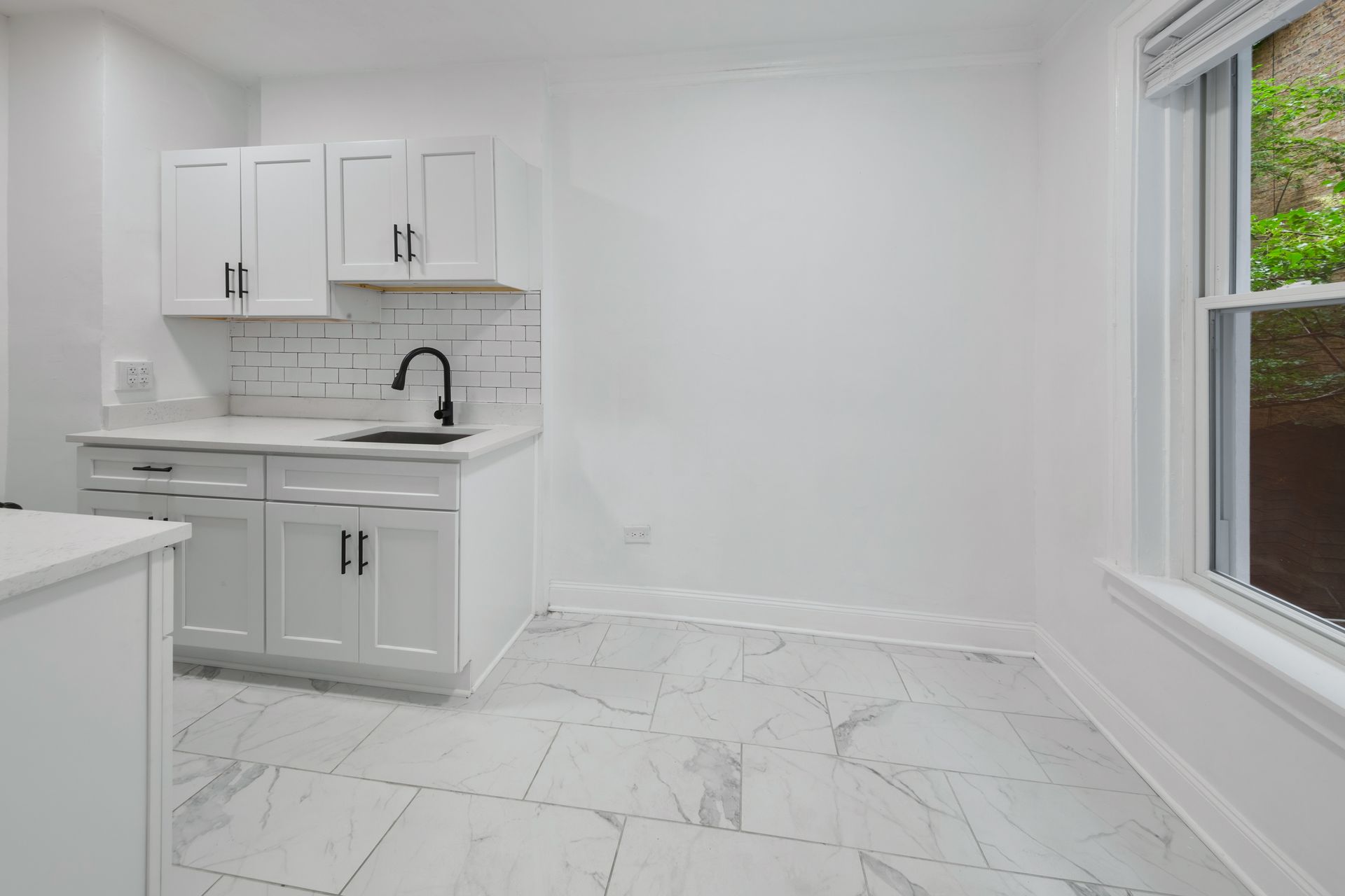White kitchen with cabinets, black faucet, and marble-look floor. Window on right.