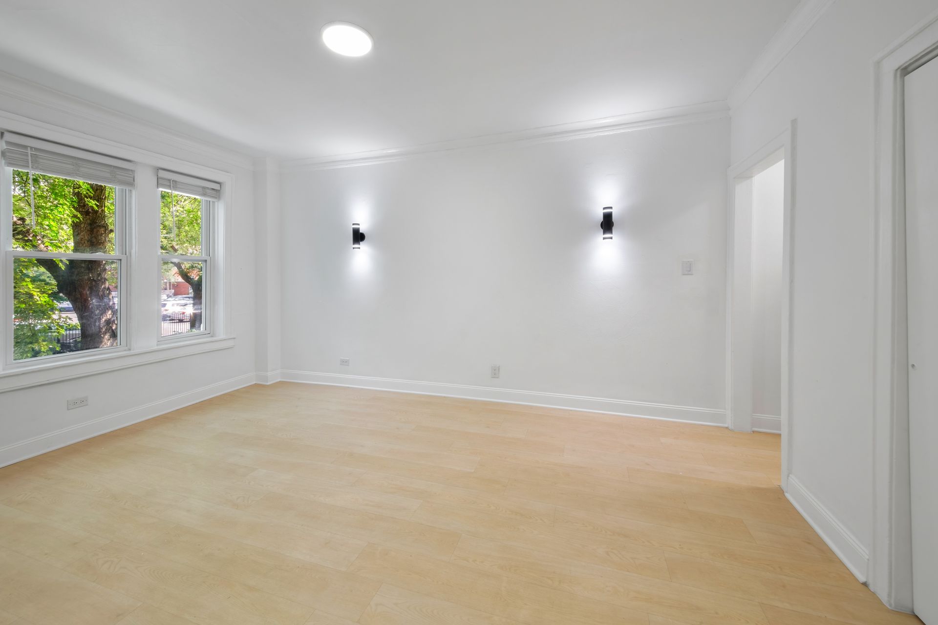 Empty room with beige carpet, white walls, two sconces, and a large window.