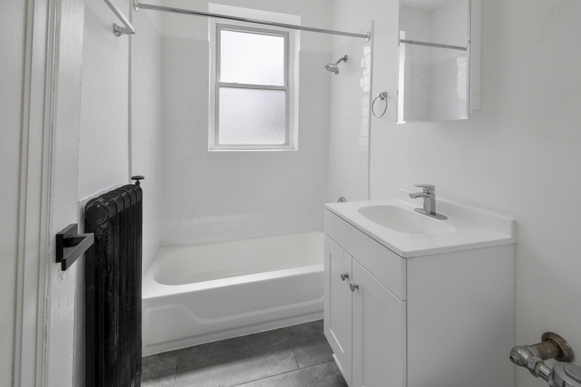 White bathroom with tub, sink, and window; black radiator.