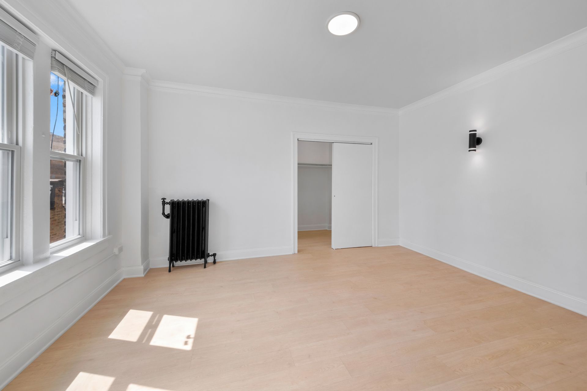 Empty, white room with beige carpet, radiator, and a closet.