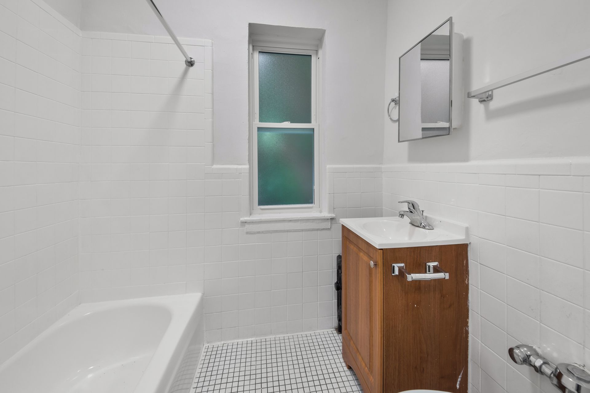 White bathroom with a bathtub, vanity, and window. White subway tile, and patterned floor tile.