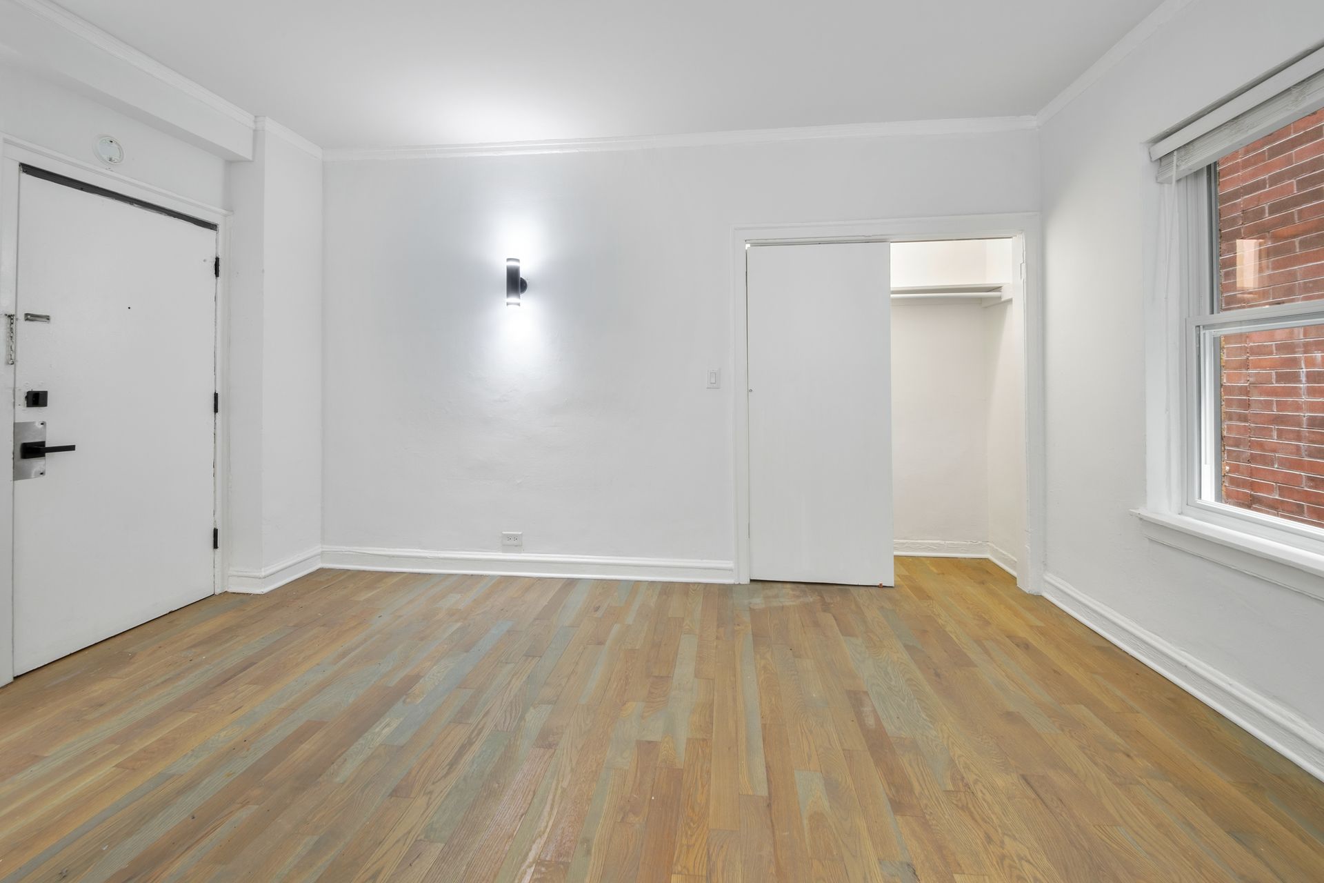 Empty room with wood floors, white walls, closet, and window.