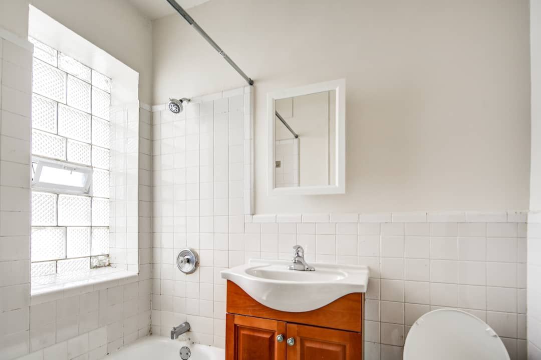 White bathroom with wood vanity, glass block window, and medicine cabinet.