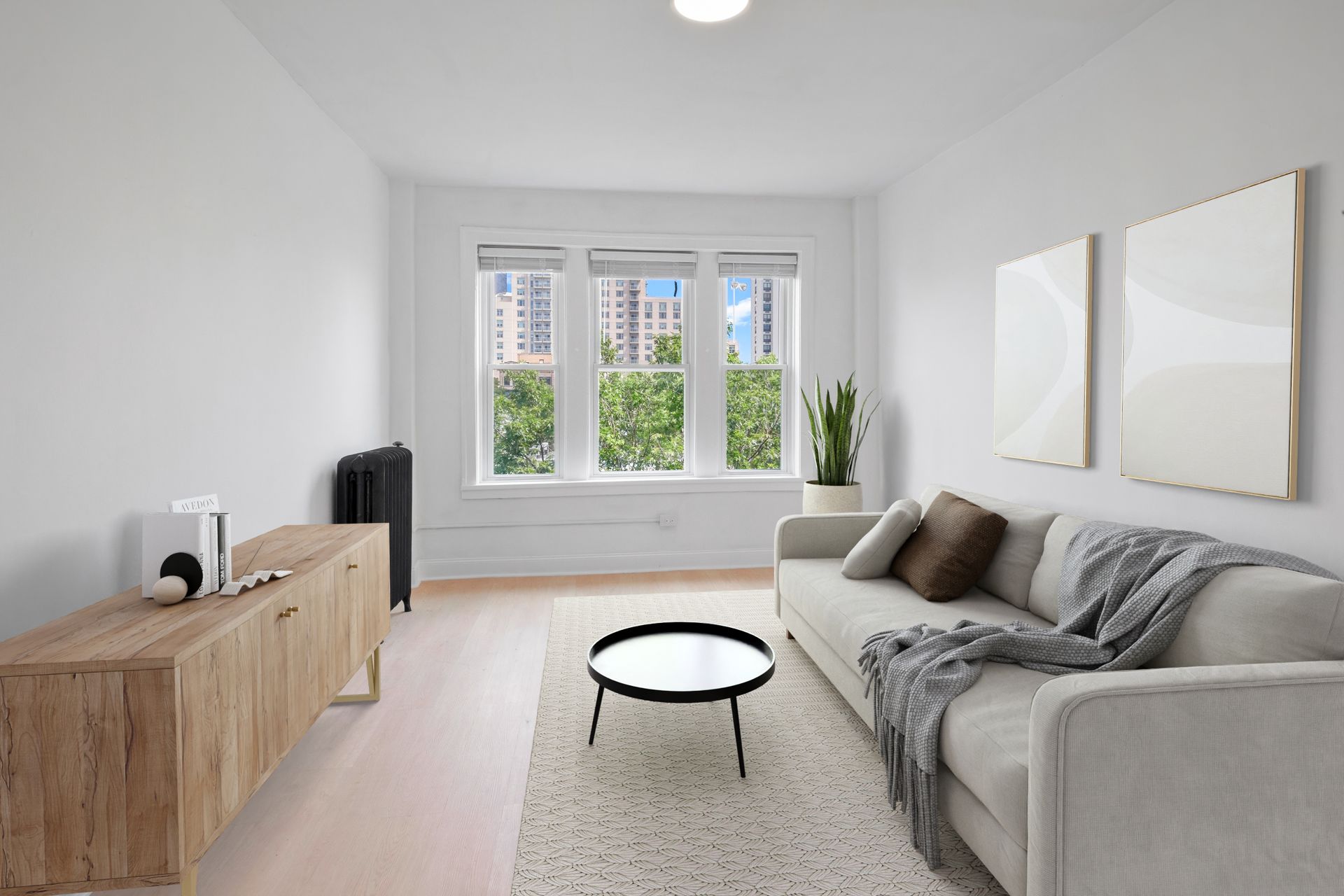 Living room with a light-colored sofa, coffee table, wooden cabinet, and windows with a city view.