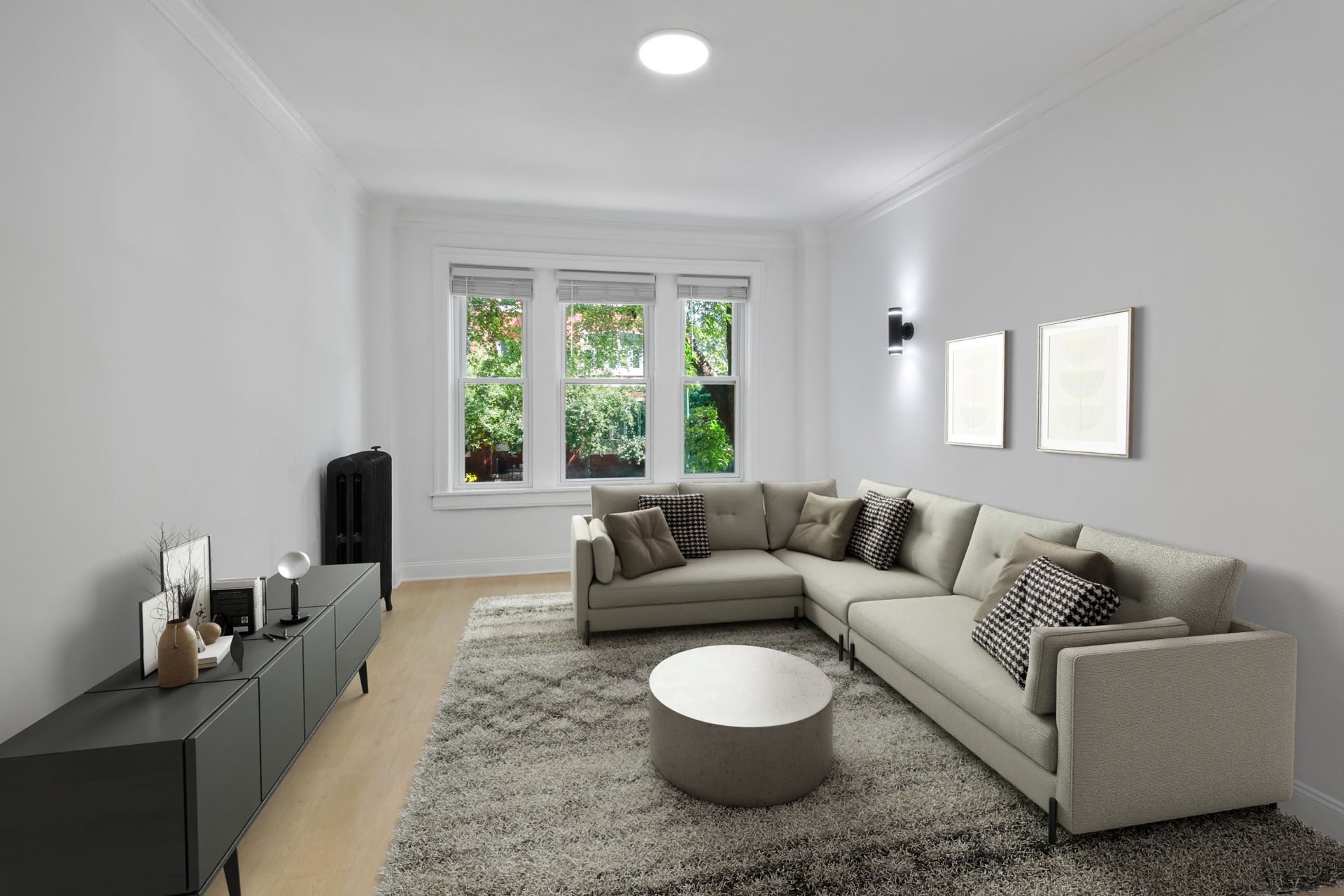 Living room with gray sectional sofa, rug, and entertainment center, next to windows with greenery.