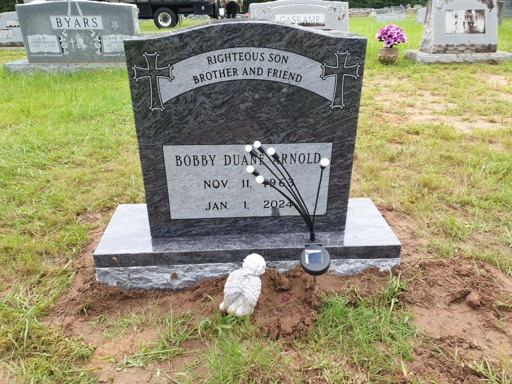 A gravestone in a cemetery with a statue of a sheep in the dirt.