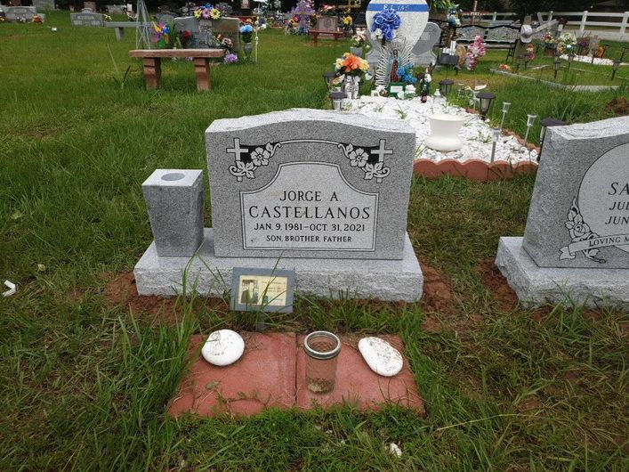 A grave in a cemetery with a vase and a cup on the ground.