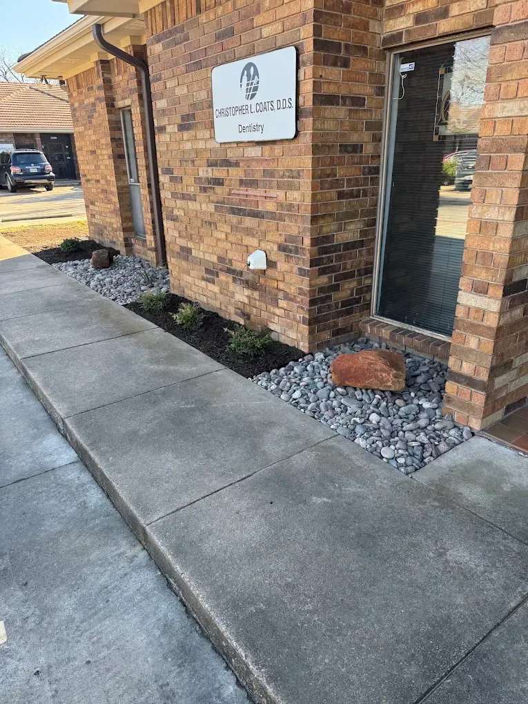 Exterior of a brick building with a concrete walkway and landscaped beds of rocks and plants.