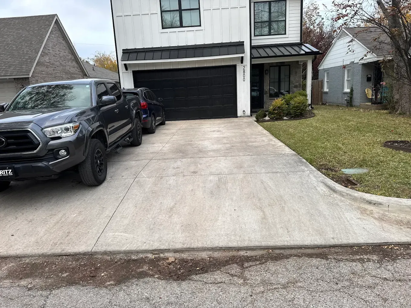 Gray pickup truck parked in a concrete driveway in front of a modern two-story white house with a black garage door.