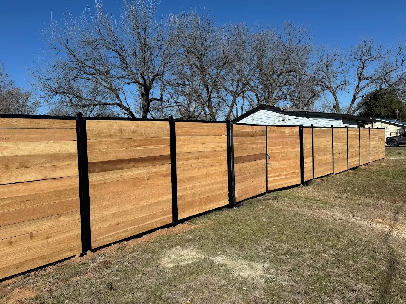 Horizontal wooden fence with black vertical posts under a blue sky.