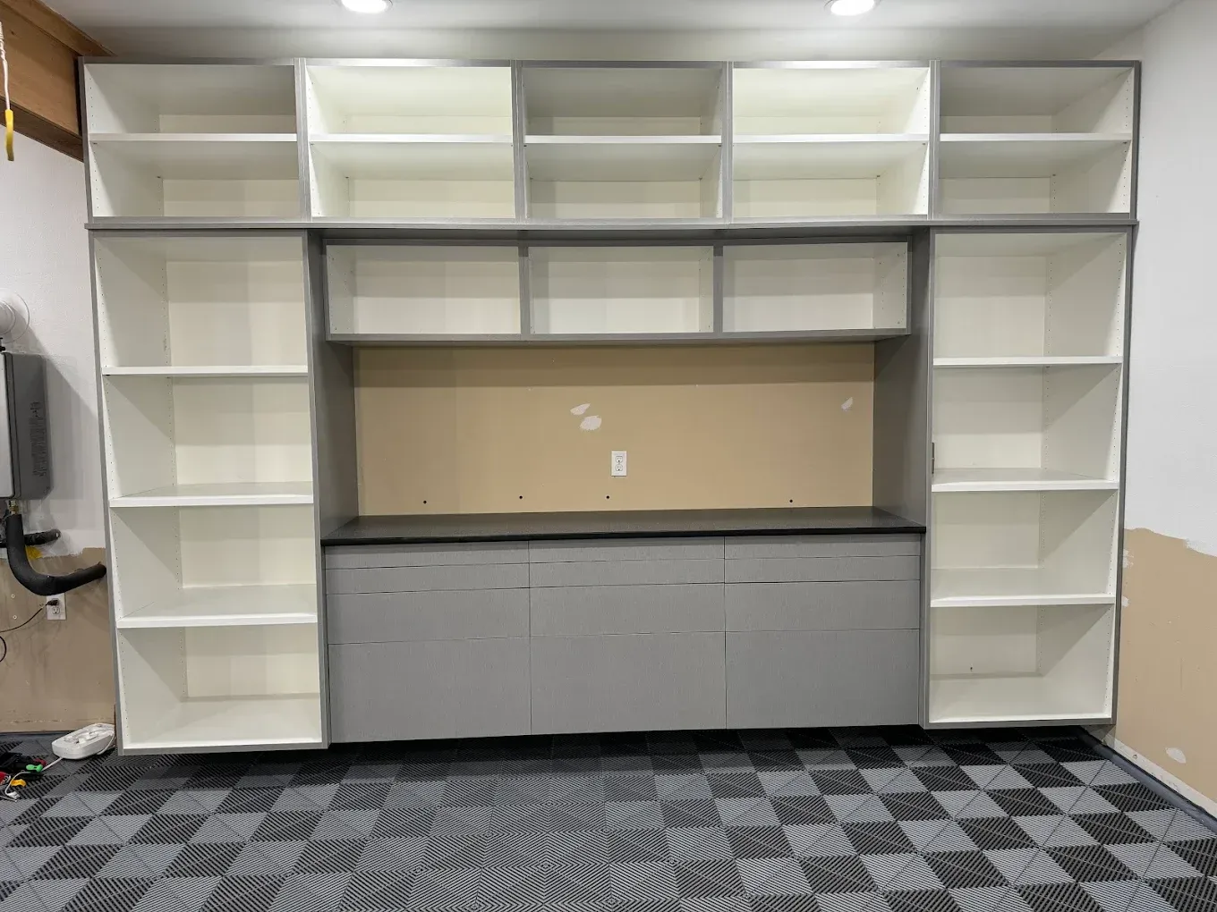 Built-in storage unit with shelves and cabinets in a garage, featuring a gray and white color scheme.