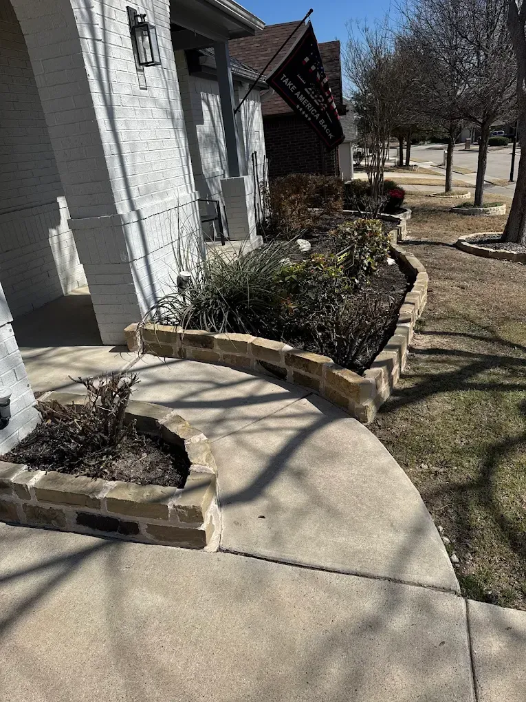 Curved concrete walkway and brick planter beds in front of a house.