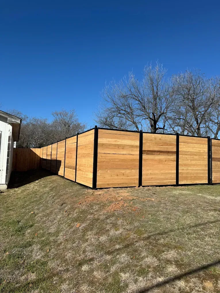 Wooden fence with black frame in a grassy yard under a blue sky.