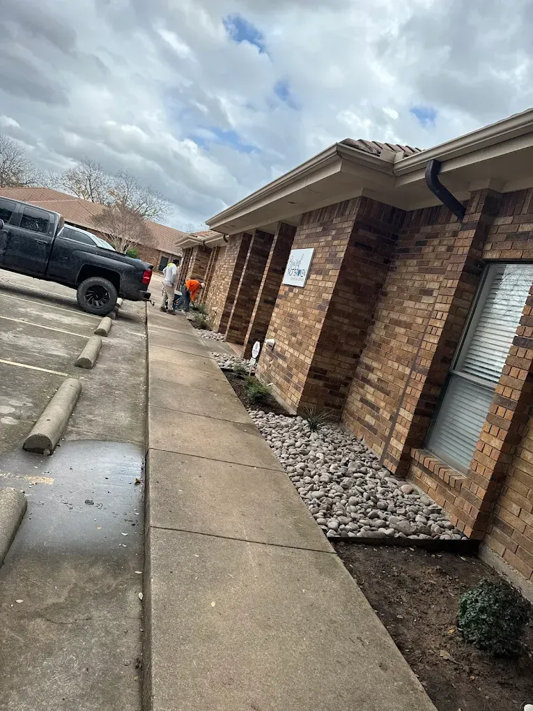 Brick building with sidewalk, rock landscaping, and parked truck on a cloudy day.