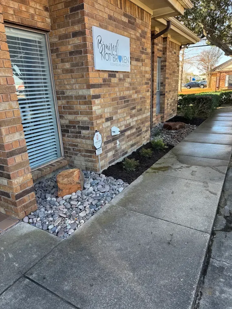 Exterior of a brick building with a sidewalk and newly landscaped area with plants and rocks.