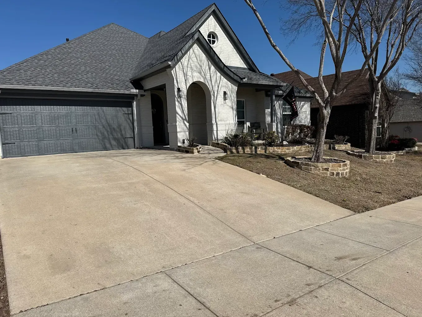 House with gray roof, white stone facade, and concrete driveway on a sunny day.