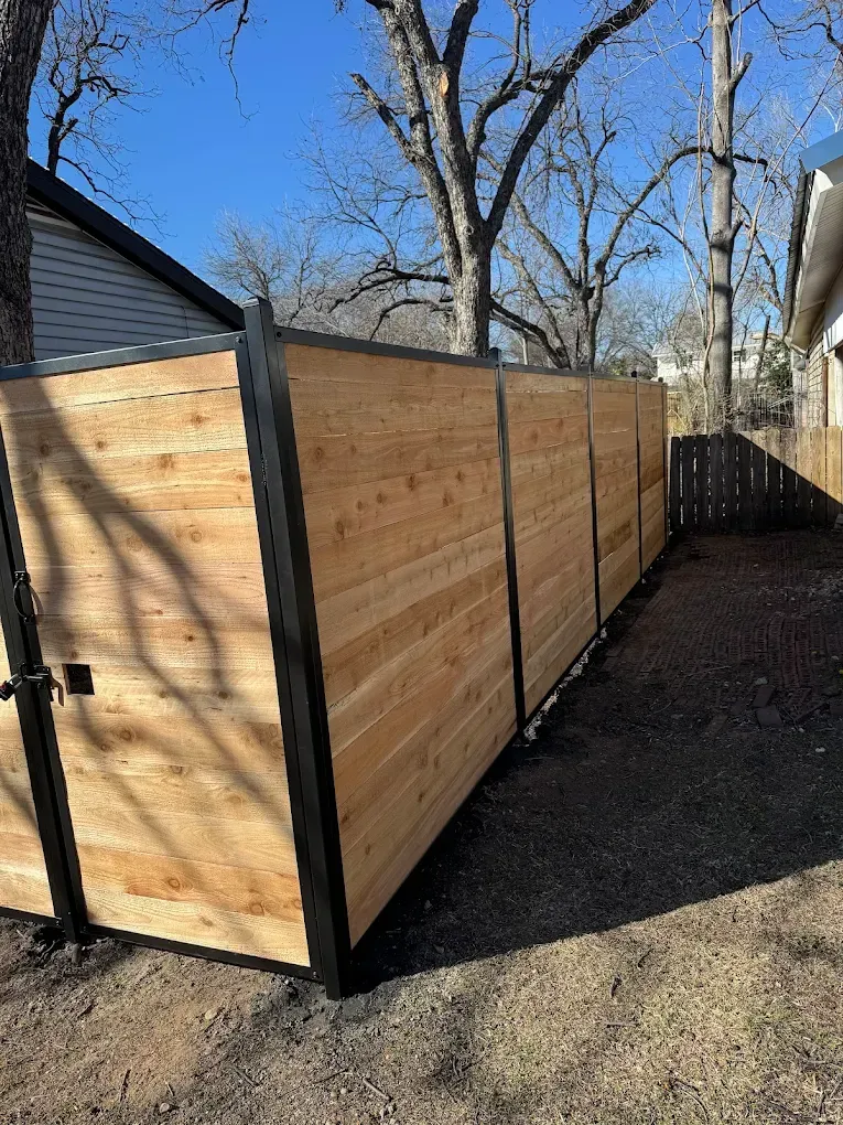 Wooden fence with black frame, next to a yard, under a blue sky.