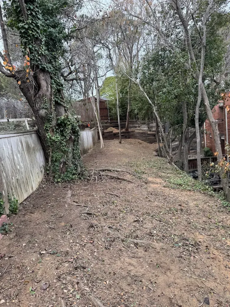 A dirt path winds through trees and beside a wall.
