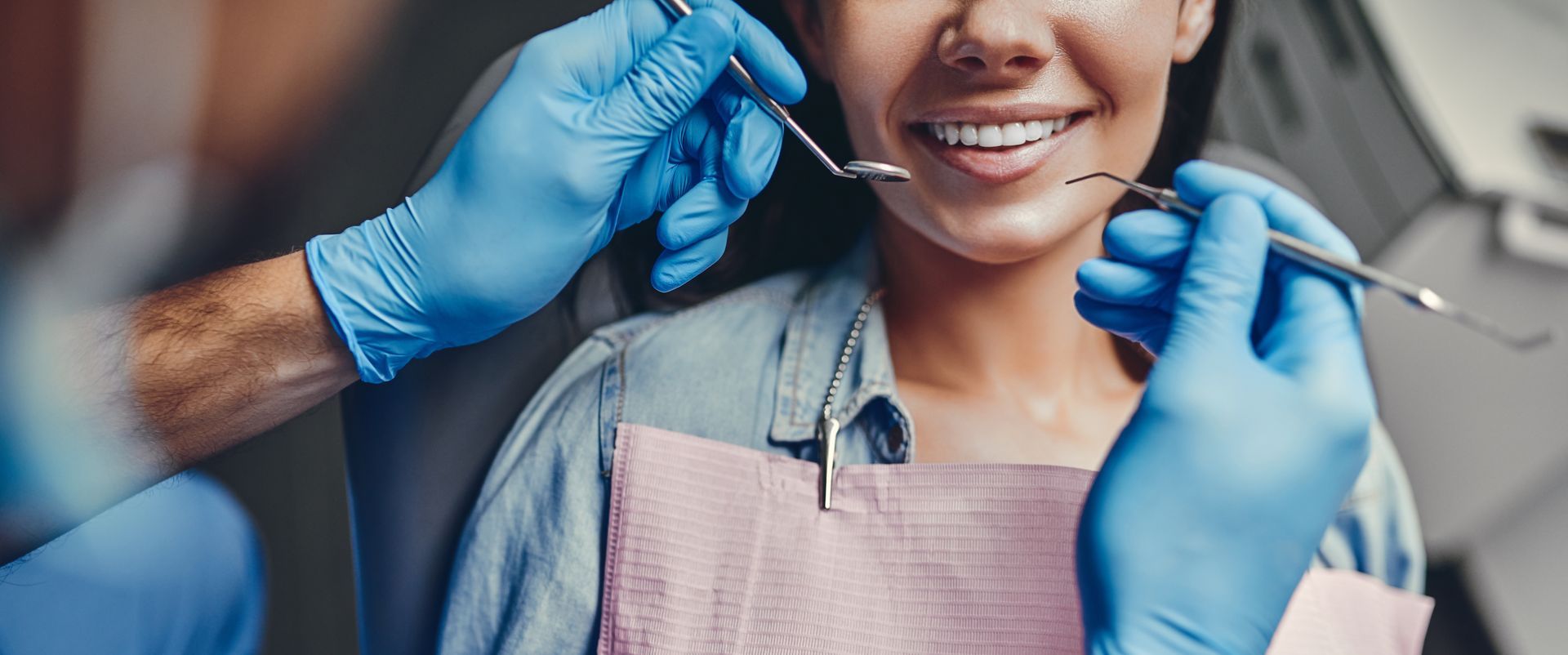 Dentist using dental tools to examine a patient wearing a pink bib.